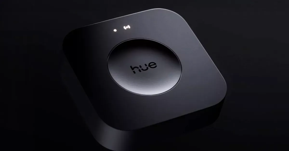 Philips Hue Bridge connected to a router with multiple Hue bulbs active in the background.