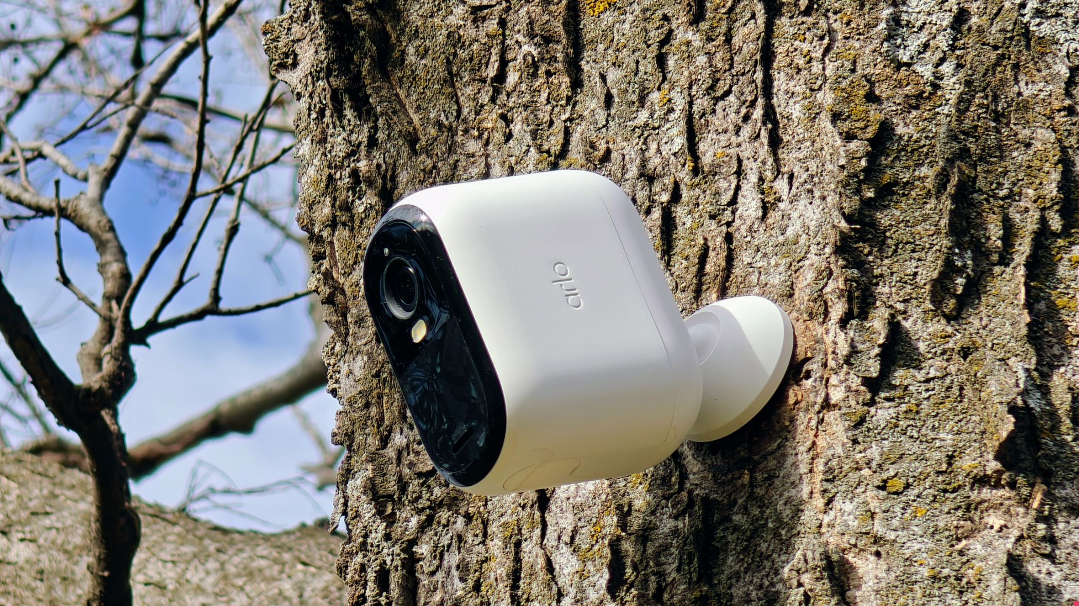 An Arlo security camera mounted outdoors with a smartphone showing the live view.